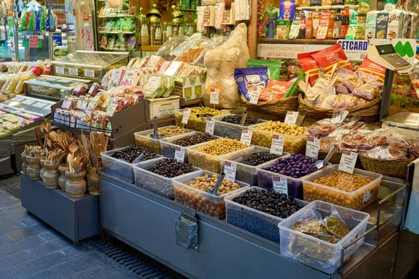 Hareketli bir piyasa sahnesi canlı zeytin ve diğer yiyecekleri sergiliyor. Sepetler ve kaplar taze ürün ve mallarla dolup taşıyor..