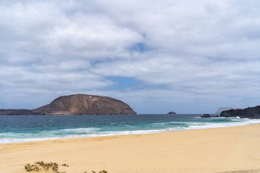 Turkuaz suları ve dağlık La Graciosa adası olan kumlu bir sahil manzarası. Kumsal güneşli..
