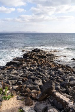Lanzarote 'nin kayalık kıyı şeridi güzel bir günde parçalı bulutlu bir gökyüzünün altında Atlantik okyanusuyla buluşuyor.. 