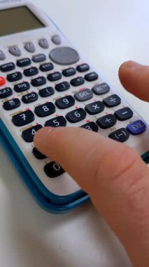 Bir kişi parmağı, karmaşık matematik için arayüz ve fonksiyon tuşlarını vurgulayan modern bir bilimsel hesap makinesinde bir düğmeye basıyor