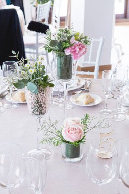 Dekorasyon olarak pembe güller ve yeşil yapraklarla dolu bir düğün masasının ayrıntıları.