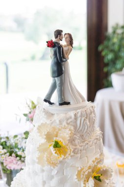 Düğün masasında süslü çiçeklerle süslenmiş güzel bir düğün pastasının tepesindeki yeni evli bir çiftin ayrıntıları.