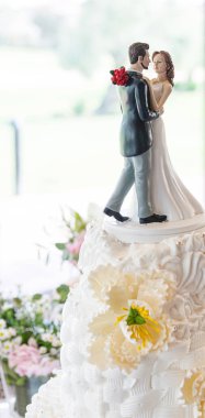 Düğün masasında süslü çiçeklerle süslenmiş güzel bir düğün pastasının tepesindeki yeni evli bir çiftin ayrıntıları.