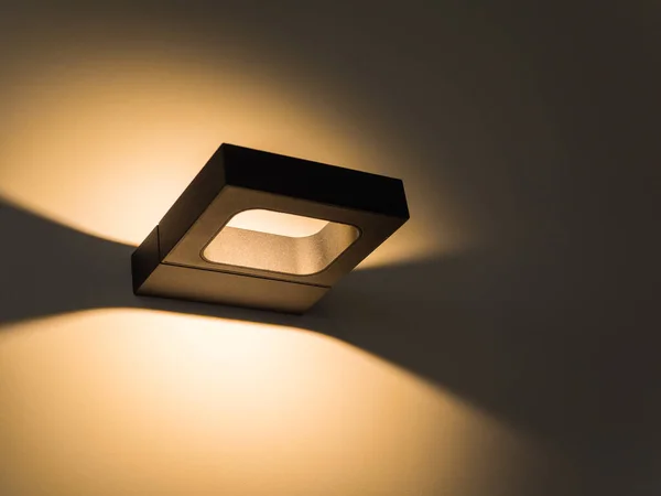Sconce. Modern minimalist black square wall lamp shines with yellow light. Internal lighting. Close-up. Beautiful geometric shadows