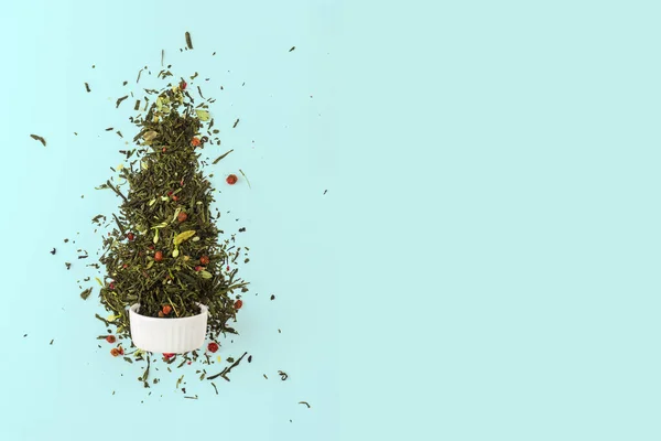 Árbol de Navidad hecho de hojas de té verde seco con bayas rojas sobre un fondo azul. Concepto de Año Nuevo mínimo con espacio de copia — Foto de Stock