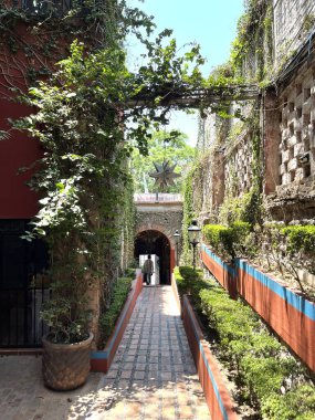 Güneşle sırılsıklam olmuş, dar bir geçitin dikey çekimi uzak uçtaki karanlık, kemerli bir geçide götürüyor.