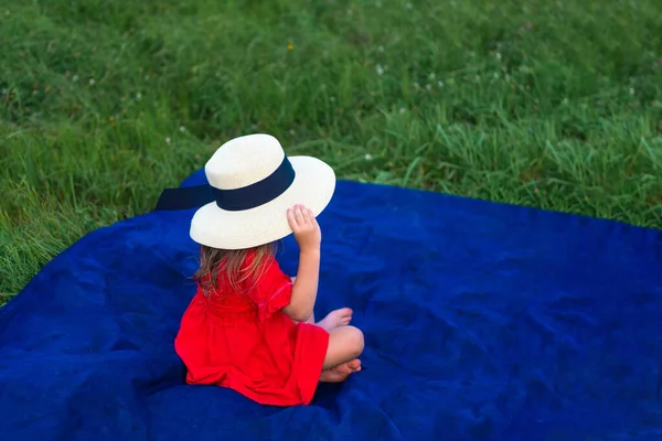 Girl in a hat and in a red dress sunbathes on the green grass. No face —  Fotos de Stock