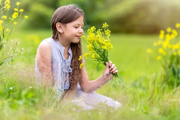 Una chica con el pelo largo en un campo oliendo flores amarillas —  Fotos de Stock