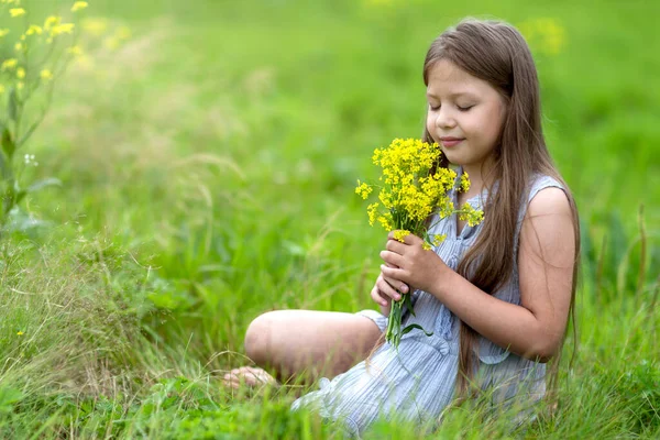 Una chica con el pelo largo en un campo oliendo flores amarillas —  Fotos de Stock