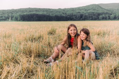 İki mutlu kız kardeş samanlıkta oturmuş sarılıyorlar.