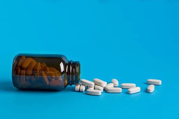 Tablets or pills of vitamins or health supplements aimed to prevent covid and other diseases in brown glass bottle against blue background. Image with copy space, horizontal orientation