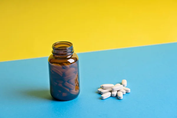 Tablets or pills of vitamins or health supplements aimed to prevent covid and other diseases in brown glass bottle against yellow and blue background. Image with copy space, horizontal. Modern concept