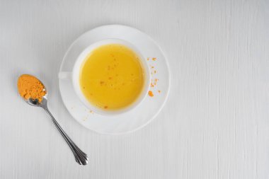 Sağlıklı olan altın ya da zerdeçal sütle dolu en üstteki bardakta beyaz ahşap arka planda bir kaşık körfez ile servis edilen antiinflamatuar özellikler var. Kopyalama alanı olan resim