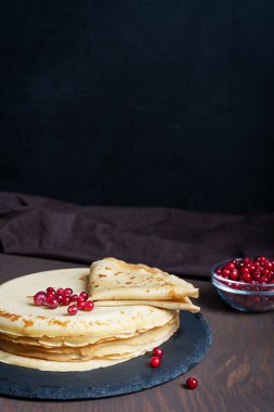 Yuvarlak taş tepside servis edilen yuvarlak, kahverengi ahşap masada yenmeye hazır kırmızı böğürtlenli Rus ev yapımı krep yığınları veya ince krepler. Kopyalama alanı olan resim, dikey