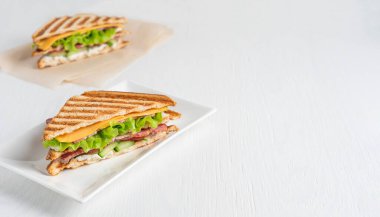 Salatalık, et ve peynirden yapılmış ev yapımı sulu sandviçler, tabakta servis edilen kızarmış ekmek dilimleri arasında marul ve mutfakta beyaz ahşap arka planda sunulan kağıt üzerinde. Kopyalama alanı olan resim