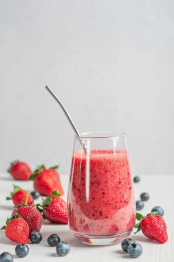 Pürüzsüz, sulu, kırmızı çilek ve yaban mersininden yapılmış taze organik smoothie ya da mutfaktaki beyaz ahşap masada yeniden kullanılabilen metalle servis edilen uzun bardakta içilen yaban mersini.