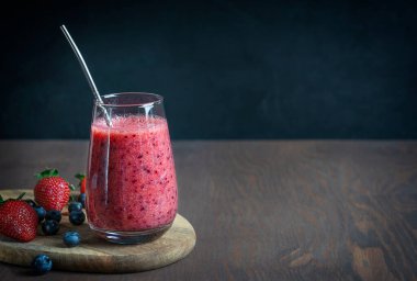 Sulu çilek ve yaban mersininden yapılmış organik smoothie siyah duvara karşı koyu kahverengi ahşap masada yeniden kullanılabilir metal pipetle servis ediliyor. Kopyalama alanı olan resim