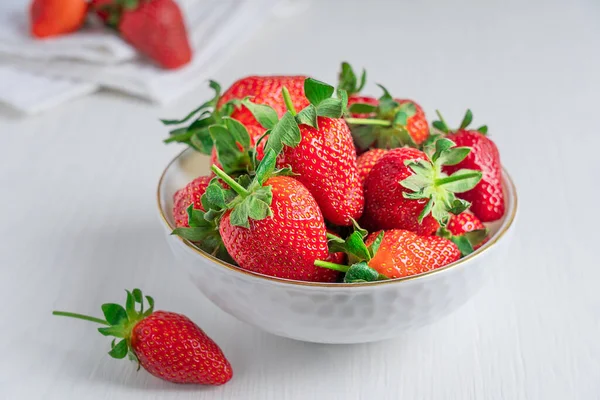 Fresh ripe scented garden strawberries with bright red color, juicy texture and sweetness, source of vitamin C and dietary minerals served in bowl on white wooden background with textile at kitchen