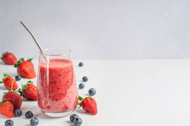 Beyaz ahşap masa üzerinde yeniden kullanılabilir metal pipetle servis edilen uzun bardakta servis edilen taze, olgun tatlı, sulu çilek ve yabanmersinlerinden yapılan organik smoothie içeceği. Kopyalama alanı olan resim