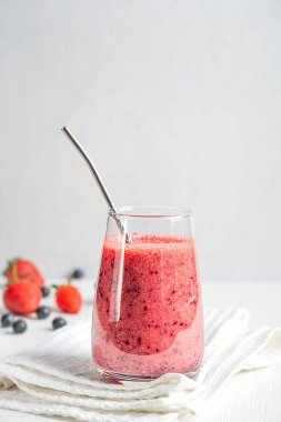 Taze vejetaryen smoothie kokteyli olgun, tatlı, sulu kırmızı çilekler ve uzun bardakta servis edilen, beyaz ahşap masa üzerinde tekrar kullanılabilir metal pipetle servis edilen yabanmersinlerinden yapıldı. Dikey