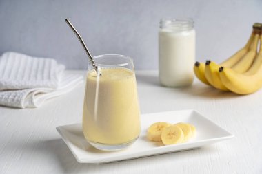 Protein enerjili smoothie veya olgun tatlı muz meyvesinden yapılmış süt karıştırılmış ve beyaz ahşap masa üzerinde sıfır atık metal kamışla birlikte içme bardağında servis edilen sütle karıştırılmış milkshake. Yatay