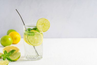 Limon ve limon dilimlerinden yapılmış ev yapımı limonata, köpüklü su ve gri duvara karşı beyaz ahşap masada metal kamışla servis edilen yeşil nane şekeri. Kopyalama alanı olan resim, yatay
