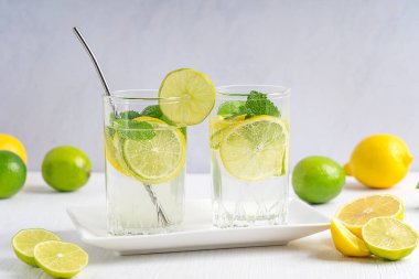 Limon ve limon dilimlerinden yapılmış taze ev yapımı organik limonata, maden suyu ve iki bardak nane şekeri gri duvara karşı beyaz ahşap masa üzerinde metal kamışla servis ediliyor. Yatay
