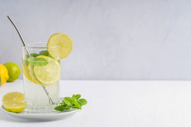 Limon ve limon dilimlerinden yapılmış soğuk limonata, beyaz ahşap zemin üzerinde metal kamışla servis edilen maden suyu ve nane yapraklarından oluşan ferahlatıcı bir içecek. Kopyalama alanı olan resim, yatay