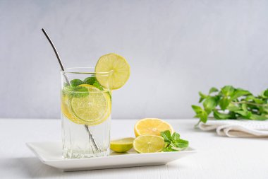Limon ve limon dilimlerinden yapılmış organik limonata, karbonatlı su ve nane yaprağı beyaz ahşap zemin üzerinde metal kamışla servis edilen içme bardağında servis edilir. Yatay