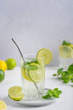 Ekşi limon ve limon dilimlerinden yapılmış taze organik limonata, maden suyu ve nane yaprağı beyaz ahşap masadaki metal pipetle servis edilen içme bardağında servis ediliyor. Dikey