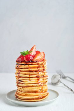 Beyaz ahşap masa üzerinde çatalla servis edilen ev yapımı Amerikan krepleri ya da çilek, nane yaprağı ve şurup sosuyla süslenmiş krepler. Kopyalama alanı olan dikey resim