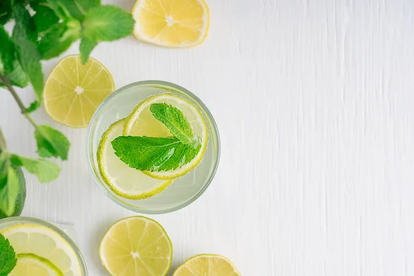 Top view on refreshing homemade lemonade made of lemon and lime slices, sparkling water and green mint leaves served in drinking glass on white wooden background. Image with copy space, horizontal