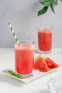 Soğuk, ferahlatıcı kırmızı karpuz taze smoothie genellikle sıcak yaz mevsimlerinde servis edilir. İçme bardağında servis edilir. Tabakta meyve dilimleri ve mutfakta beyaz ahşap masada buz küpleri ile birlikte. Dikey