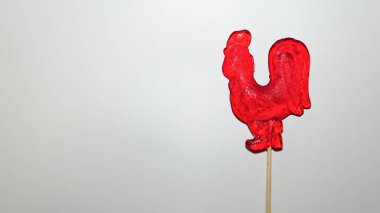Horoz şeklinde kırmızı bir lolipop. Tahta çubukta şeker lolipopu.