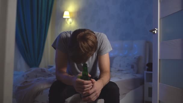 Портрет самотньої людини з депресією, що сидить на ліжку з пляшкою алкоголю — стокове відео