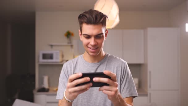 En ung mann som spiller videospill på smarttelefonen sin, vinner et veddeløpsspill i stua. Begrepet mobilanvendelse – stockvideo