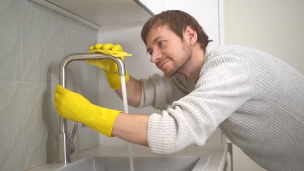 Junger Mann mit gelben Handschuhen reinigt den Wasserhahn aus Stahl in der Küche — Stockvideo