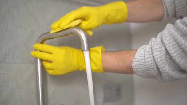 Nahaufnahme Junger Mann mit gelben Handschuhen, der den Wasserhahn aus Stahl in der Küche reinigt — Stockvideo