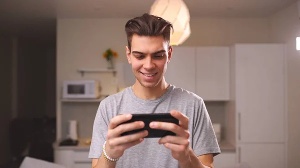 Jeune homme jouant à un jeu vidéo sur son smartphone gagner un jeu de course dans le salon. Concept d'application mobile — Photo