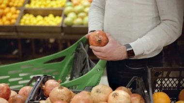 Mans el gıda rafından taze bir nar alır. Alışveriş yapan kişi markette nar seçer.