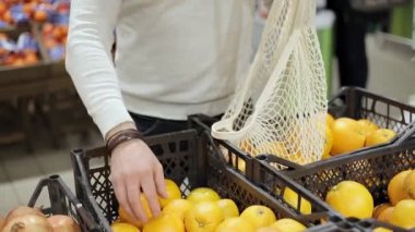 İnsan ellerine yakın çekim. Portakalları ürün mağazasında eko iplik torbasına koyuyorlar.