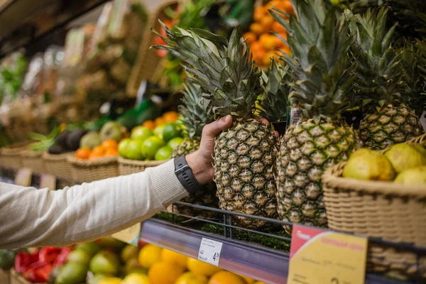 Крупним планом чоловіча рука вибирає ананас в продуктовому магазині Стокове Зображення