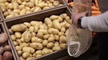 Erkek eli kapalı süpermarkette patatesleri eko torbaya koyar.