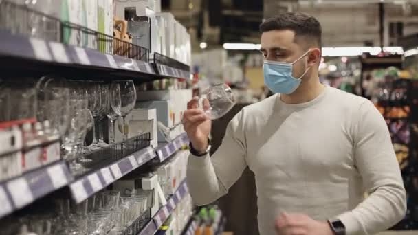 Ung man i mask väljer vinglas på heminredning butik — Stockvideo