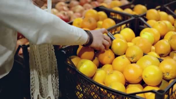 Primer plano de las manos del hombre pone naranjas en la bolsa de red ecológica en la tienda de productos — Vídeos de Stock