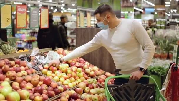 Maskeli adam yemek rafından taze bir elma alıyor. Alışveriş yapan kişi markette elma seçiyor. — Stok video
