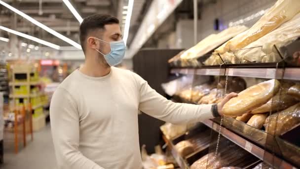 Мужчина в одноразовой медицинской маске выбирает хлеб во время покупок в булочной супермаркете. Защита и предотвращение мер во время эпидемии. — стоковое видео