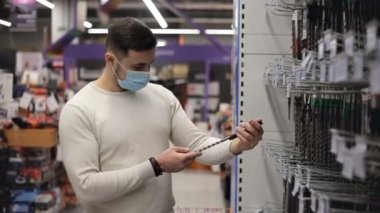 Maskeli genç adam alet deposunda beton matkap seçiyor.