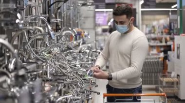 Tıbbi maske takan bir alıcı hırdavatçıdan tuvalet malzemesi alıyor. Musluk vinci ya da su musluğu dokunuyor.