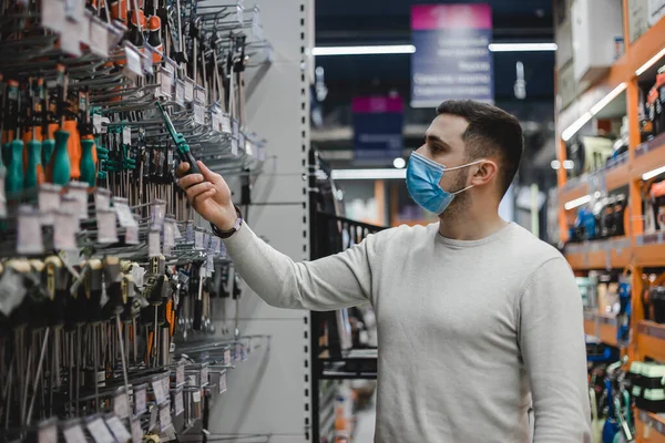 Молодой человек в одноразовой медицинской маске выбирает отвертку в магазине инструментов Лицензионные Стоковые Изображения